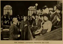 A photograph depicts a jury box full of women in elaborate hats and other early 20th century fashions