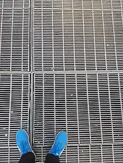close up view of subway grating with the photographer's shows in view for scale.