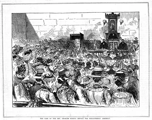 Black and white print showing a large crowd in a courtroom. In the background, a panel of three men in judges' robes can be seen.