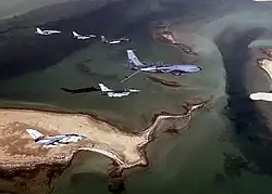 Photo of seven modern aircraft of differing designs flying in formation above a group of sandy islands