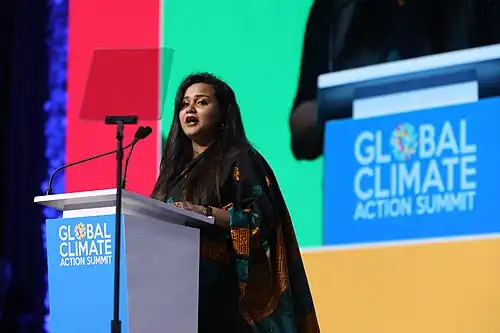 Wickramanayake is speaking at a podium, and the podium has a blue banner reading "Global Climate Action Summit"