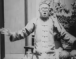 A black-and-white image of a young man wearing large spectacles, an expression of shock on his face