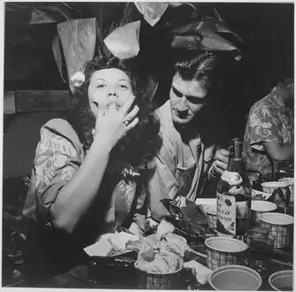 Navy pilots relax and enjoy feminine companionship, sports and entertainment at Chris Holmes Rest Home, maintained for pilots on leave from combat. Fingers replace forks at chow-time. Hawaii, March 1944.[12]