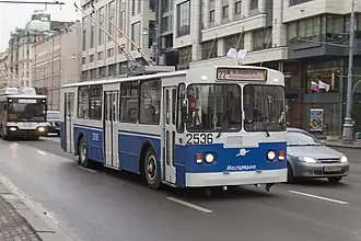 Aquamarine-and-white trolleybus under a viaduct