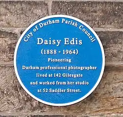 Blue plaque reading "City of Durham Parish Council. Daisy Edis (1888–1964). Pioneering Durham professional photographer lived at 142 Gilesgate and worked from her studio at 52 Saddler Street"