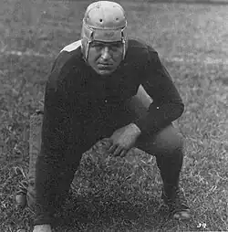 A Caucasoid man in a 1920s football helmet is posing poised for tackling.