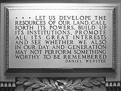 A grey marble plaque. Under the plaque are leaves, and text on the plaque reads: "RESOURCES OF OUR LAND, CALL FORTH ITS POWERS, BUILD UP ITS INSTITUTIONS, PROMOTE ALL ITS GREAT INTERESTS AND SEE WHETHER WE ALSO IN OUR DAY AND GENERATION MAY NOT PERFORM SOMETHING WORTHY TO BE REMEMBERED".