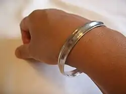 A photograph of a hand and arm with a metal religious bracelet, commonly made of iron or steel. The hand pose is relaxed and the bracelet is simple, having a shaped but not decorated design.