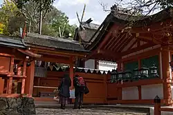 Building with white walls, red wooden beams and forked finials on the roof located behind a fence with gate.