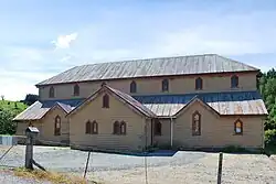 A two-storey wooden building with a rusty iron roof