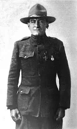 Three-quarters shot of a middle-aged man in a plain military uniform, standing almost at attention. He is wearing a campaign hat and two medals on his chest.