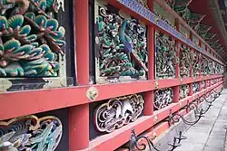 Wooden wall with red beams and colored carvings of plants, peacocks and other birds.