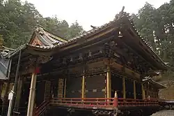 A black wooden building with gilt decorations and a veranda with a red handrail.